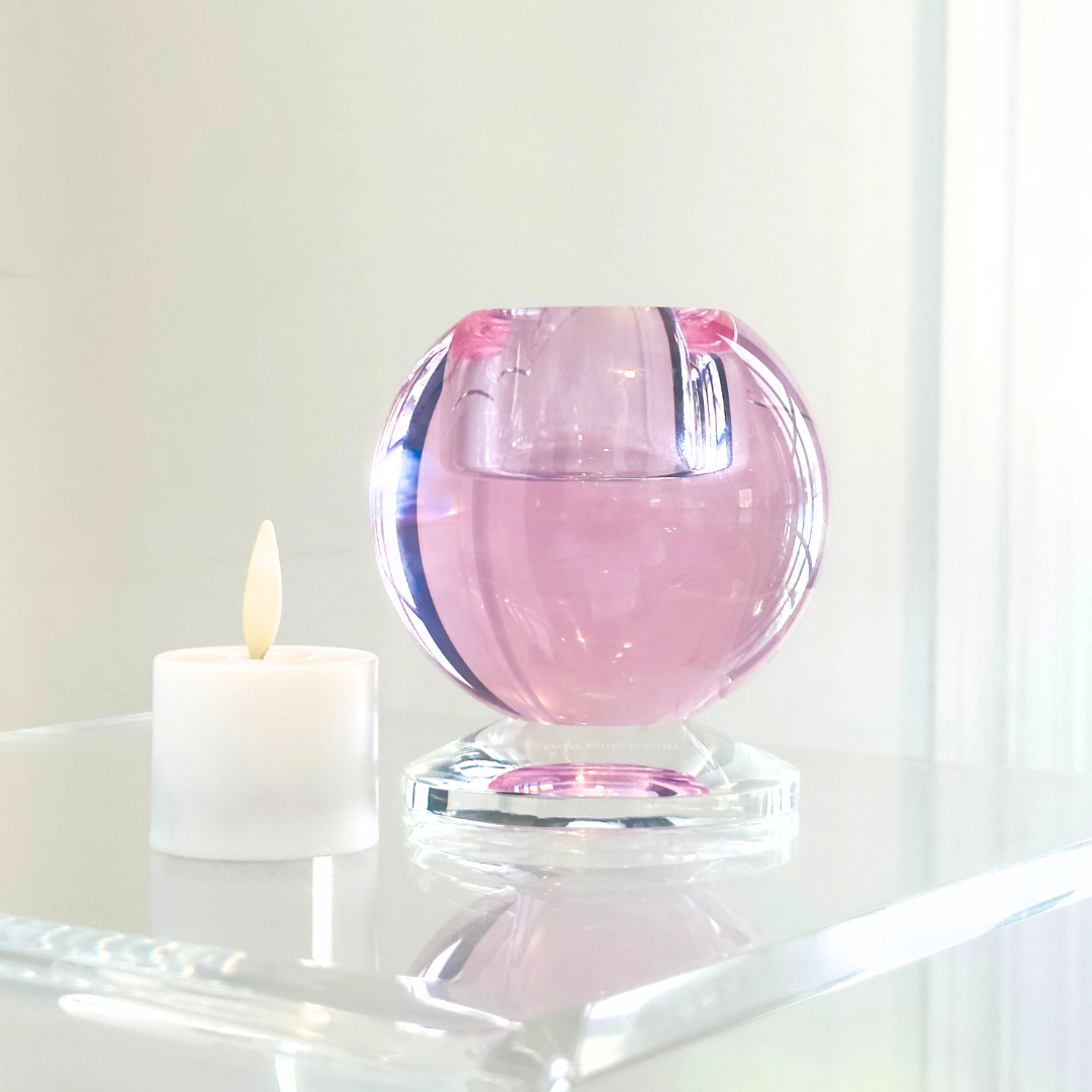 Pink crystal votive holder on a white surface with a lit votive candle on the side 