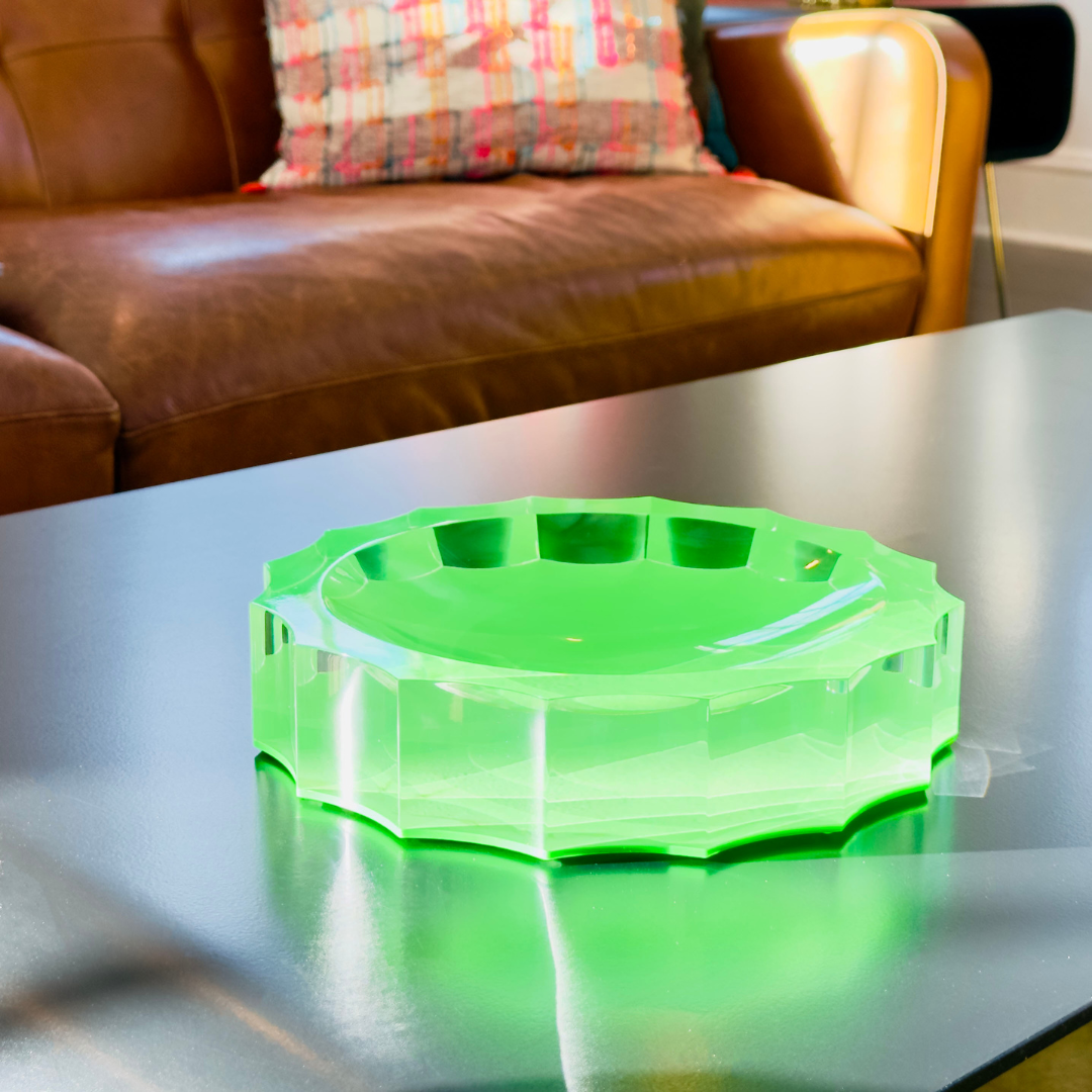 Green acrylic dish on a reflective surface with a brown leather couch in the background