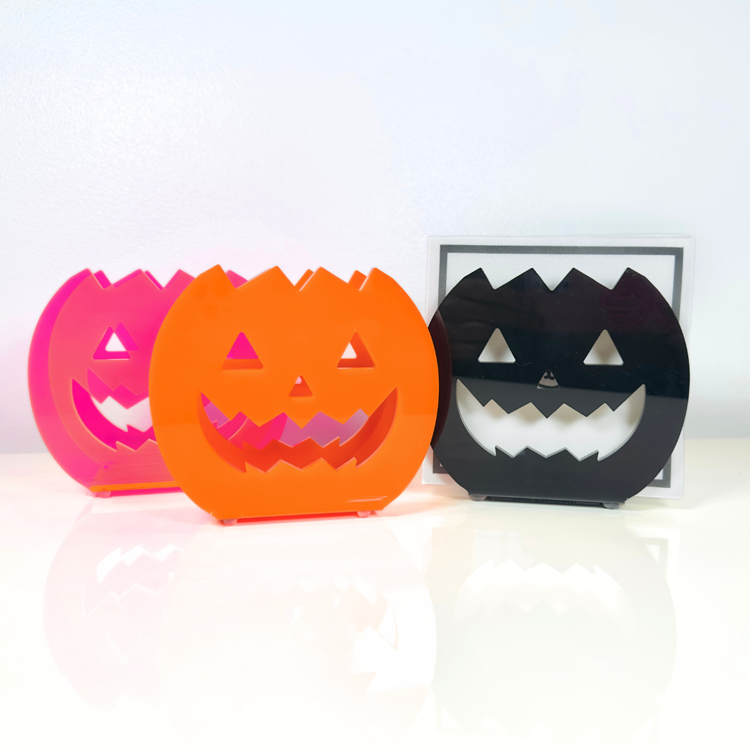Three Halloween-themed acrylic napkin holders in pink, orange, and black on a white background