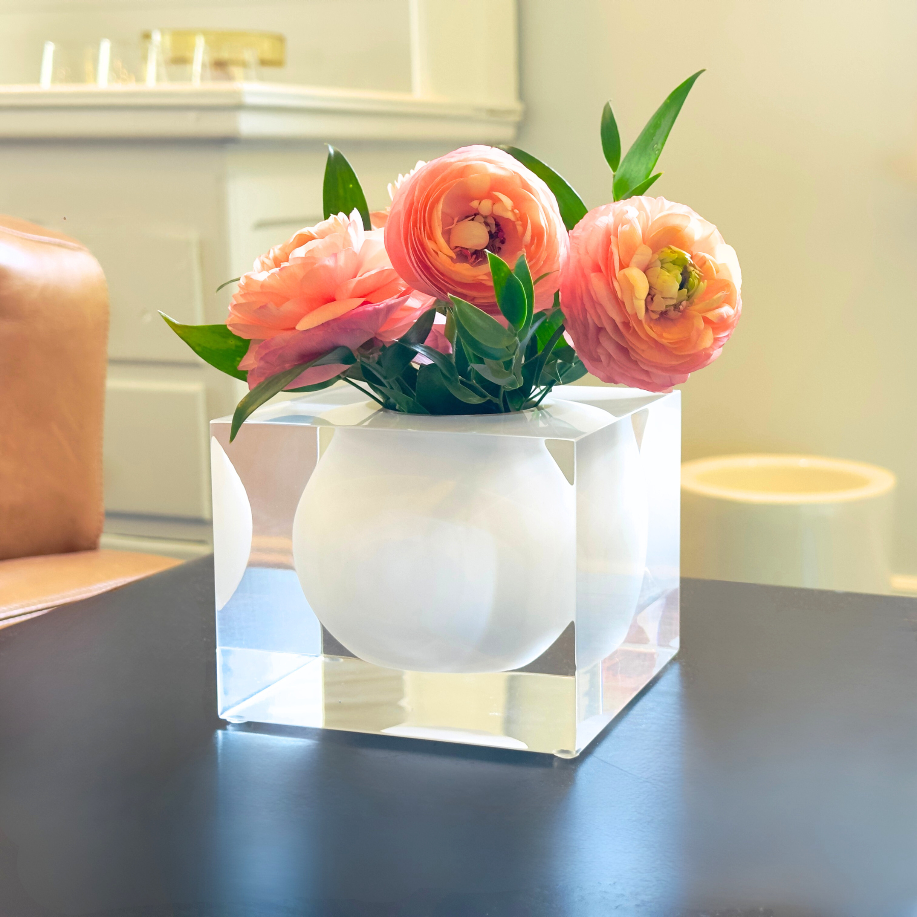 Clear acrylic block with white vase inside  containing pink flowers on a reflective surface.