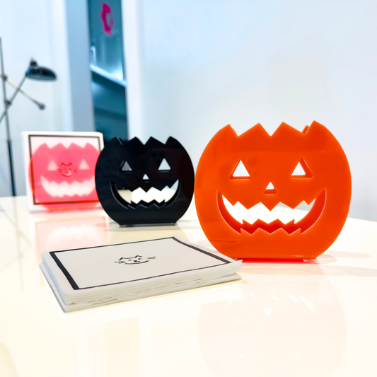 Three Halloween-themed jack-o-lantern cutouts in pink, black, and orange on a table.