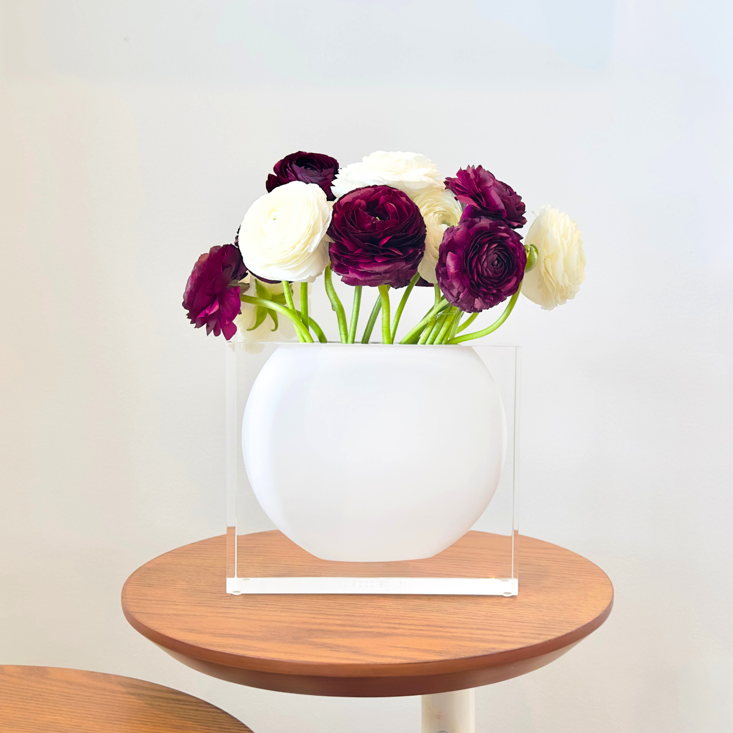 White vase with purple and white flowers on a wooden table against a light background