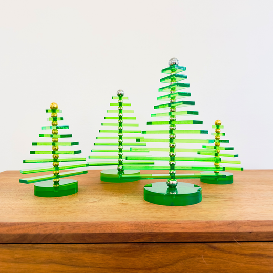 Set of four green acrylic Christmas trees on a wooden surface with a white background