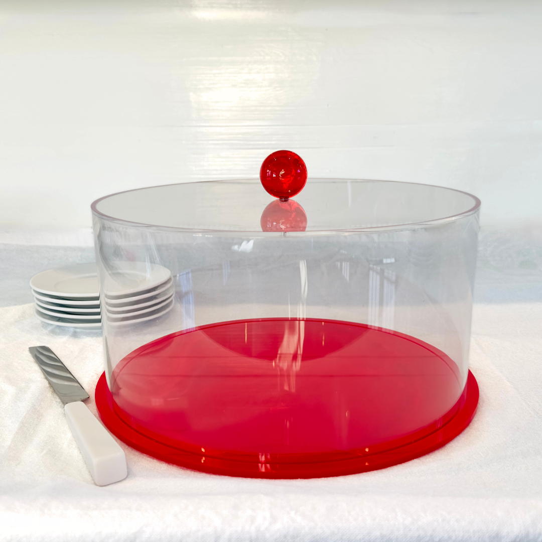 Clear acrylic cake stand with red base and red ball on a white surface