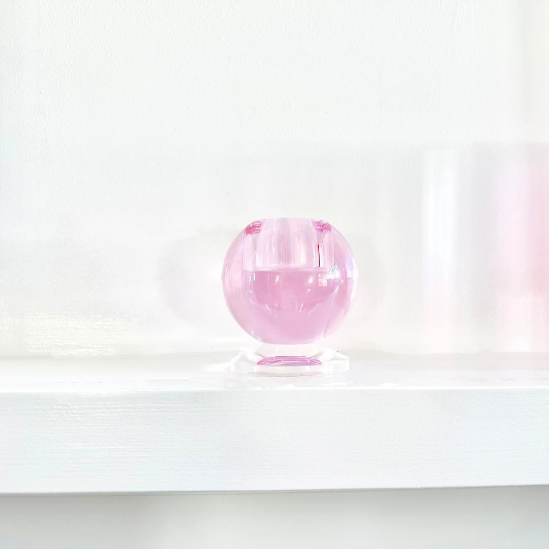 Pink crystal sphere on a white surface with a white background