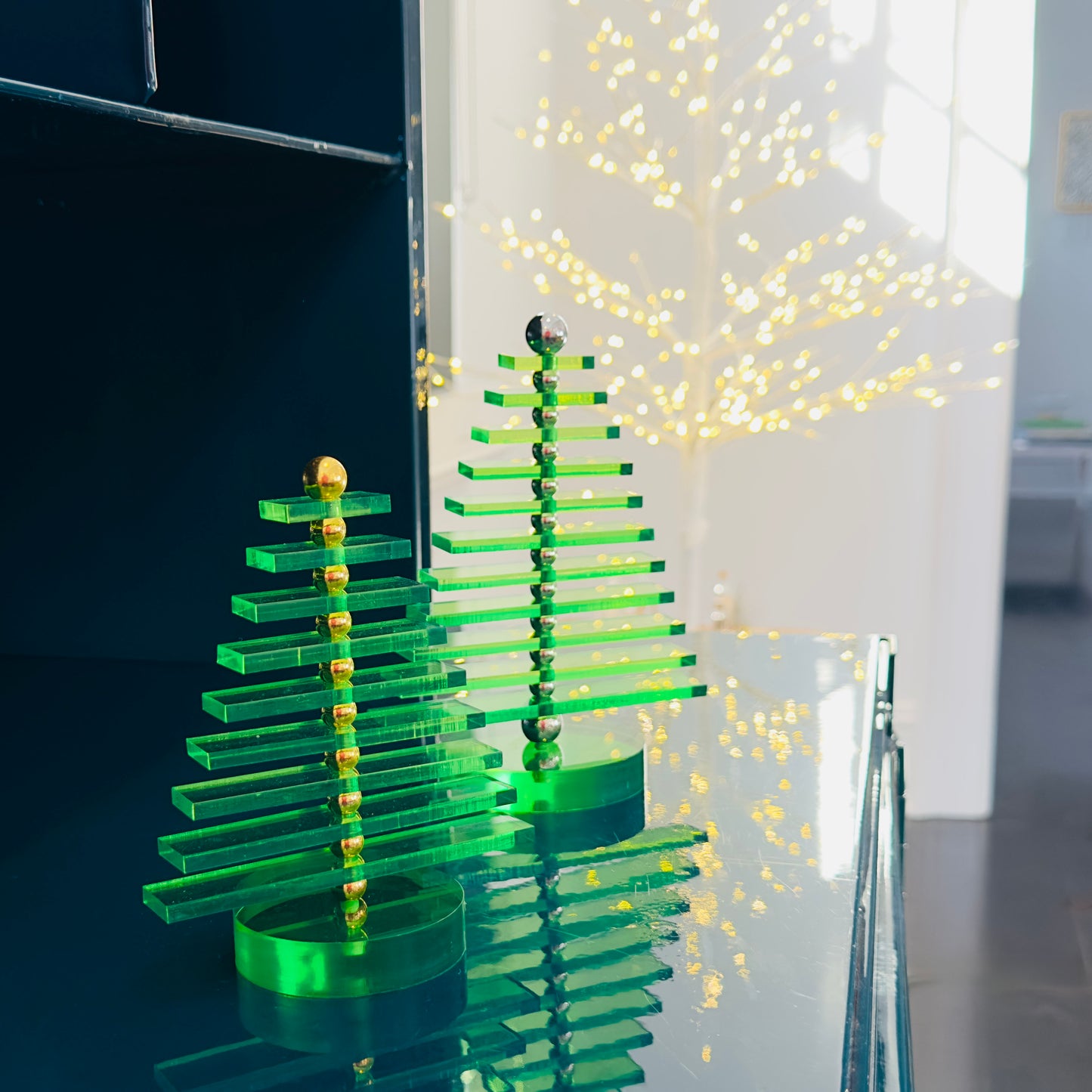 Green acrylic Christmas tree on a reflective surface with blurred lights in the background