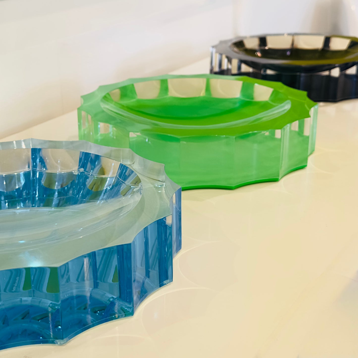 three acrylic decorative bowls, one green and one blue, one black on a white surface