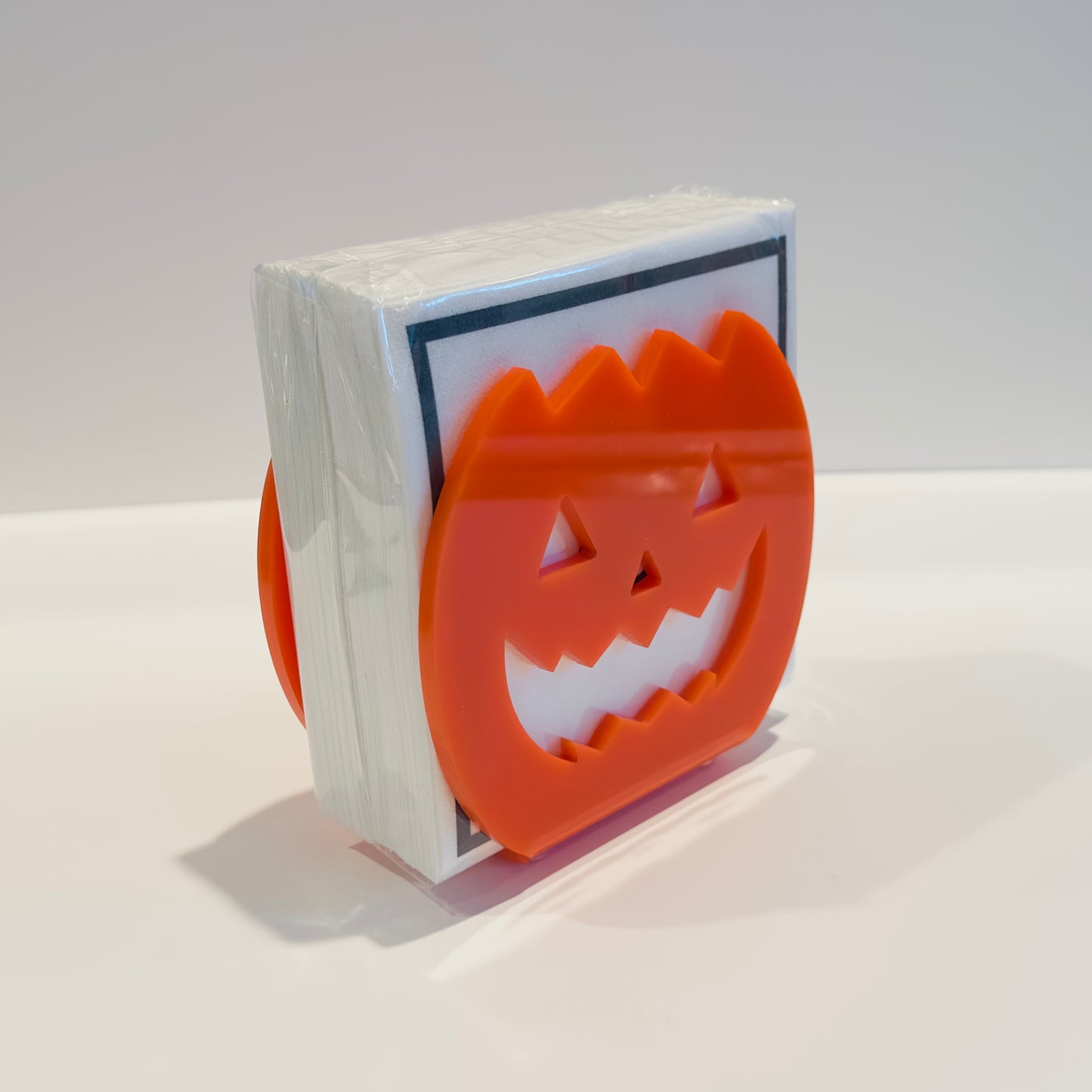 Orange jack-o-lantern napkin holder with a stack of white napkins on a white background