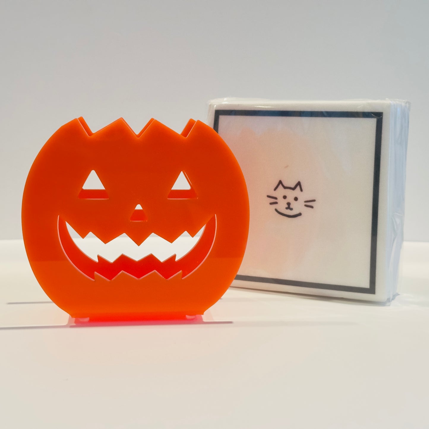 Halloween-themed paper napkins with a orange jack-o'-lantern design napkin holder on a white background