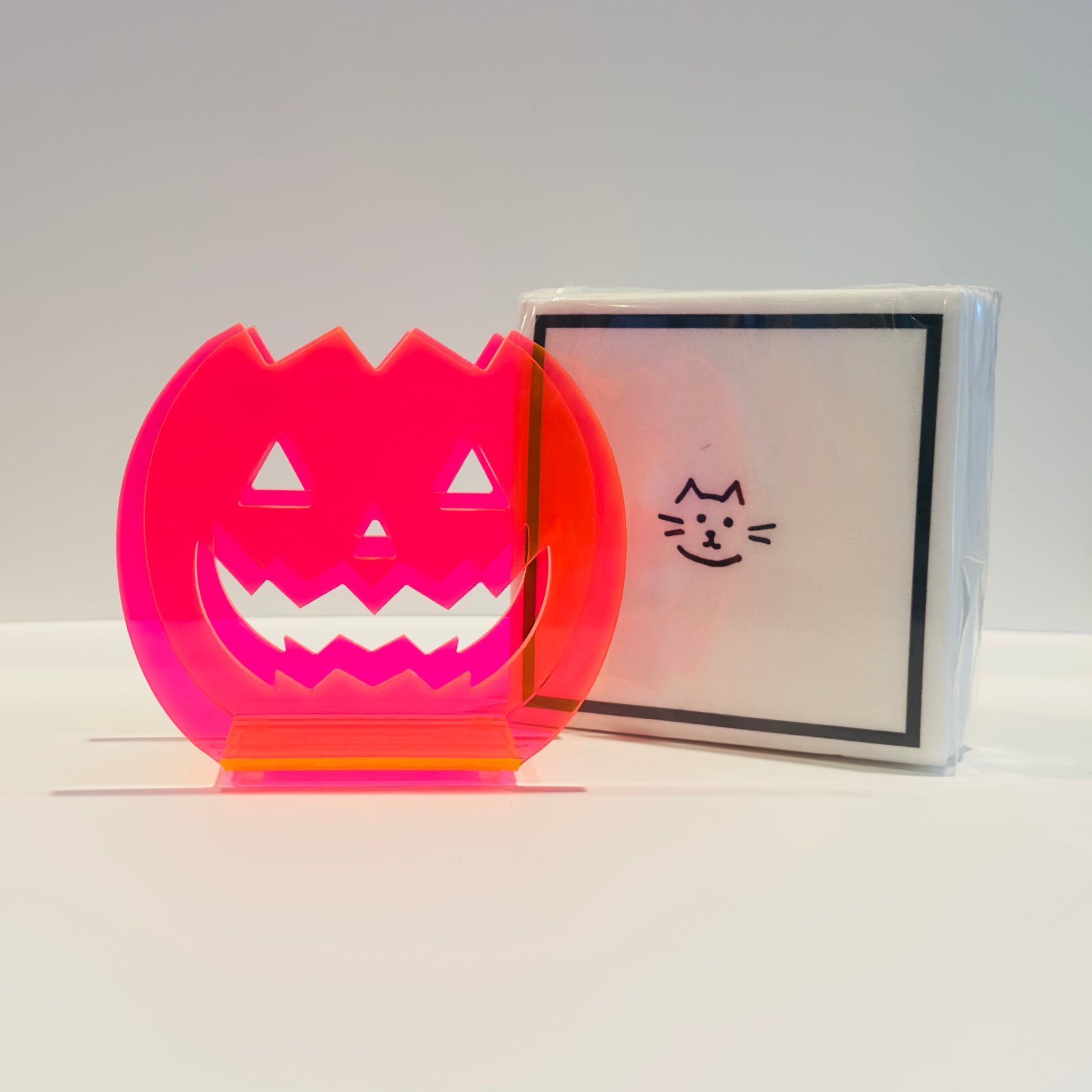 Halloween-themed paper napkins with a jack-o'-lantern design napkin holder on a white background