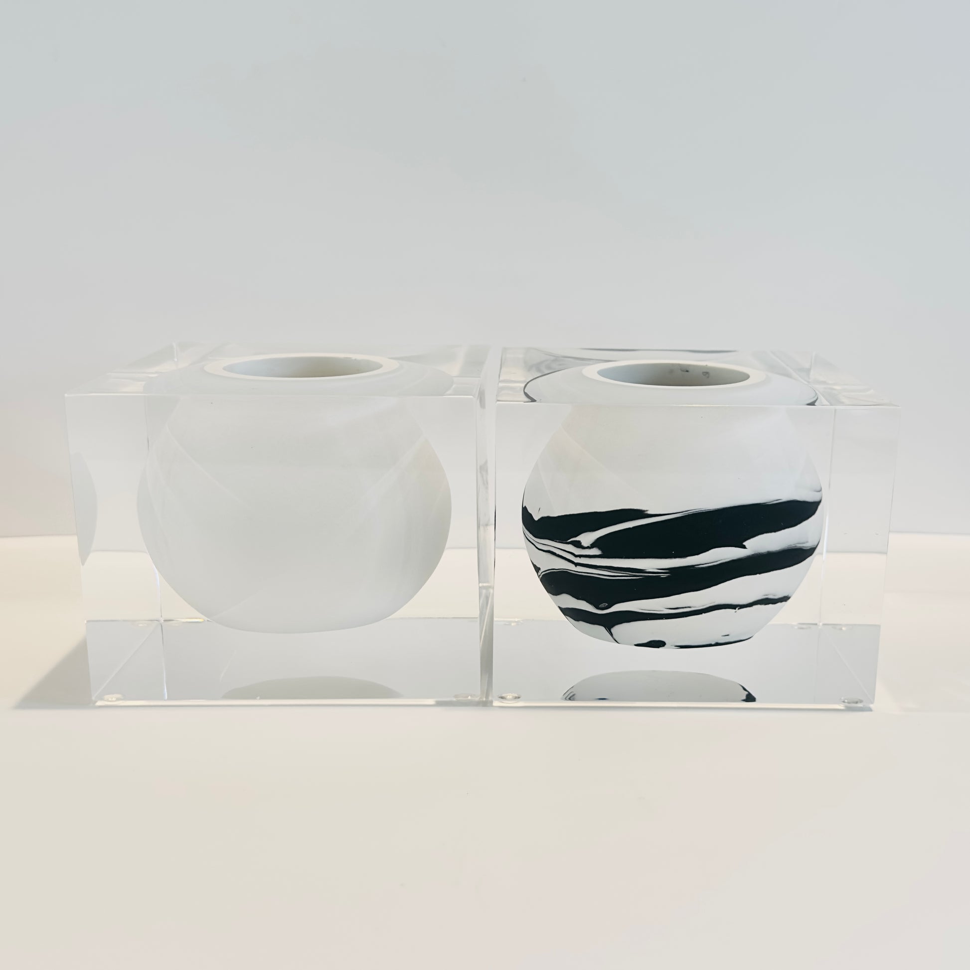 Two acrylic vases with black and white patterns  and solid white in a clear acrylic holder on a light gray background