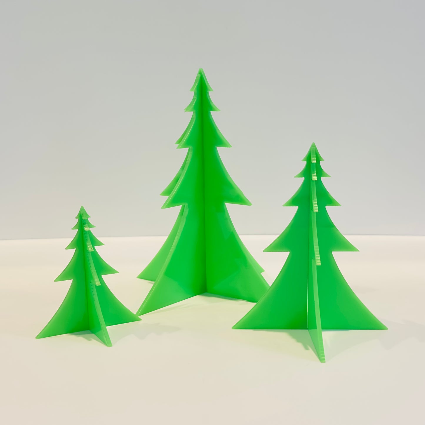 Three green Christmas tree-shaped candles on a white surface with a light gray background