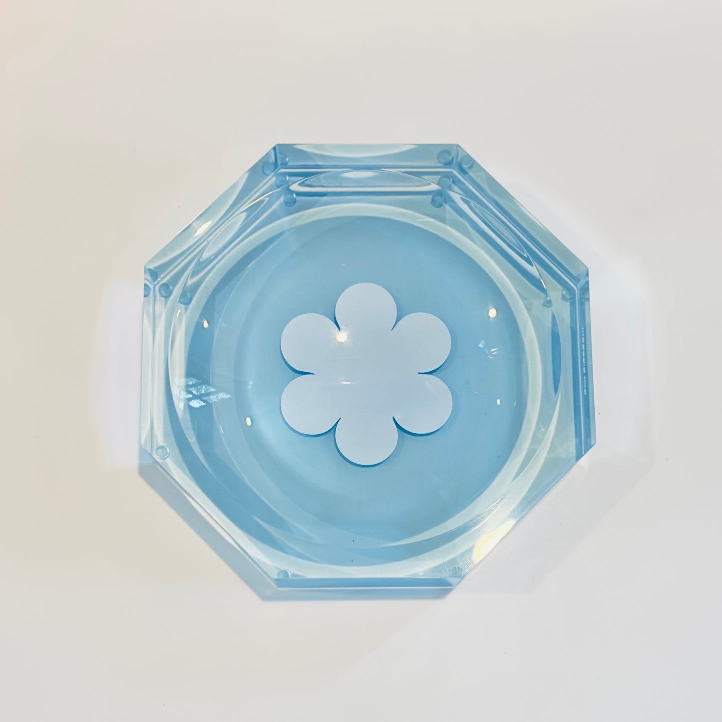 Top view of blue acrylic dish with a white flower-shaped cavity on a light gray background