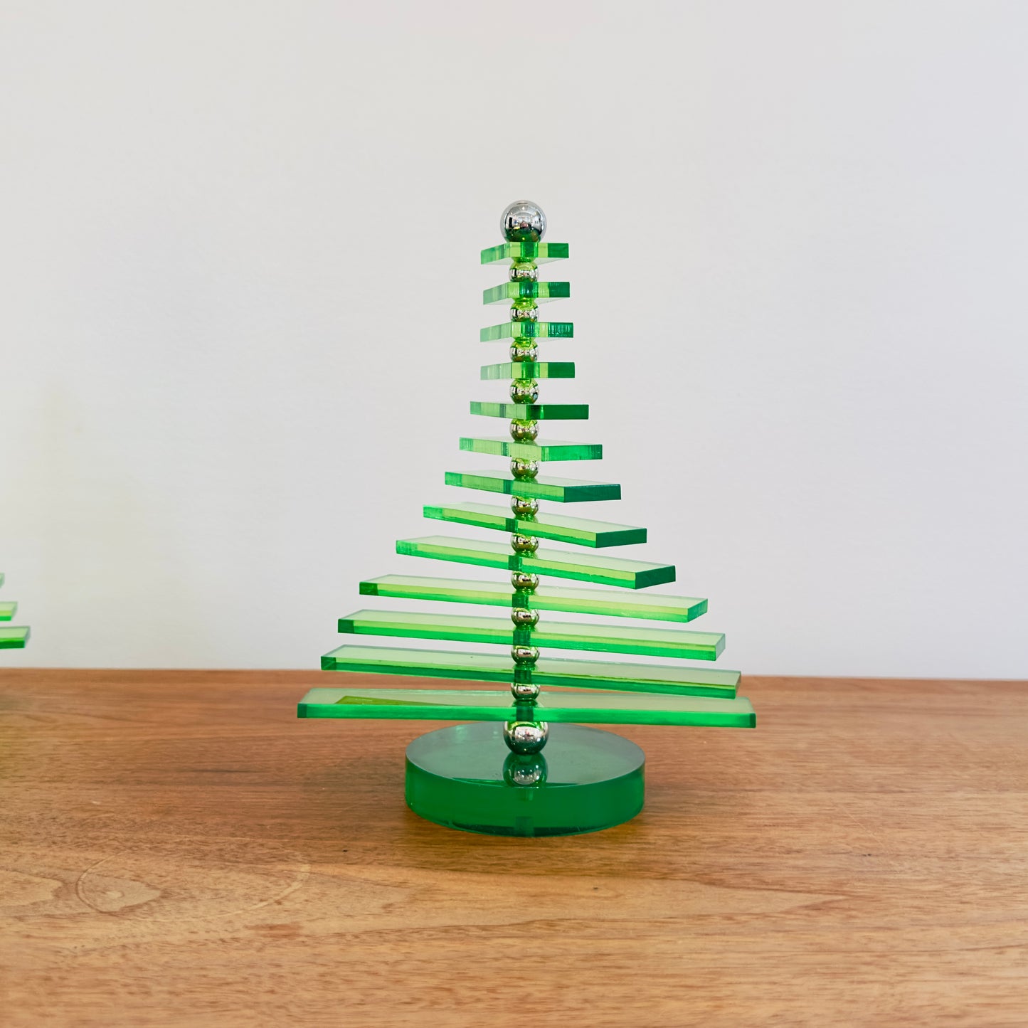 Green acrylic Christmas tree on a wooden surface with a plain background