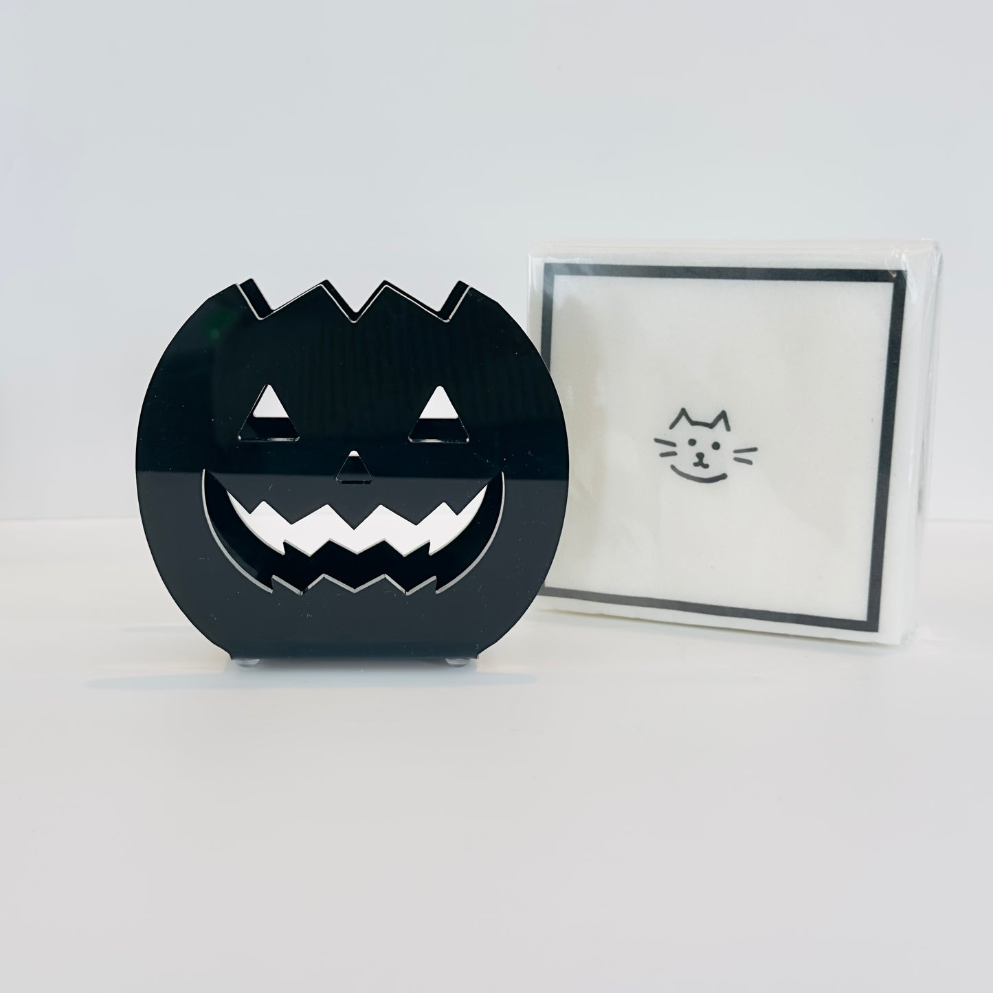 Black jack-o-lantern napkin holder with a stack of white napkins on a white background