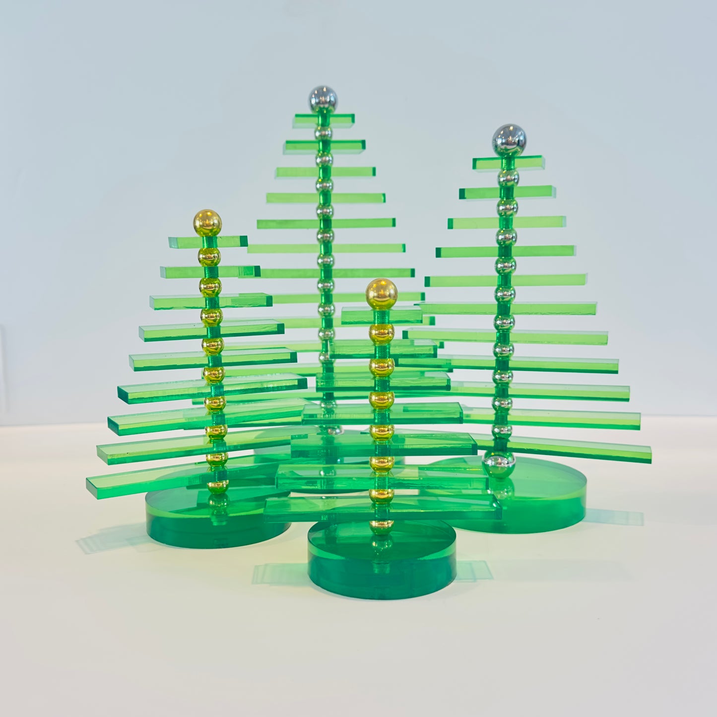 Set os four green acrylic Christmas trees with gold and silver accents on a white background