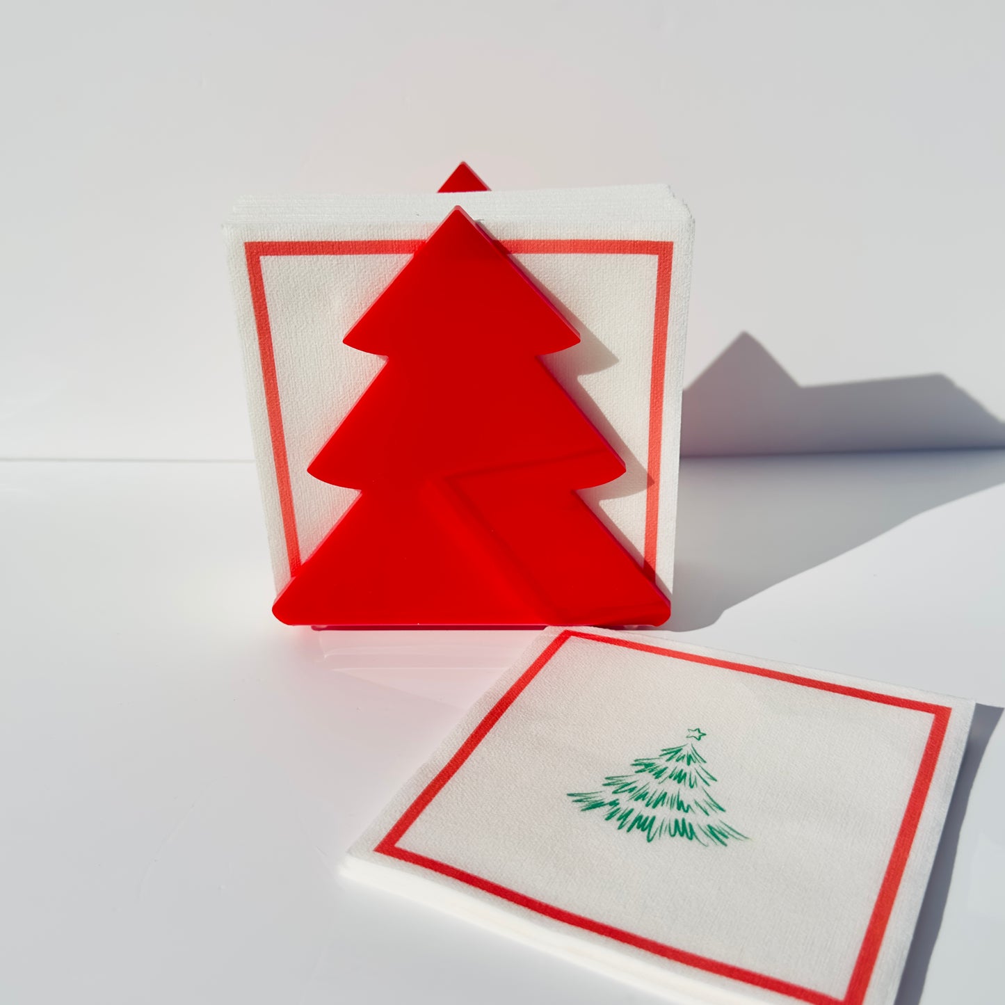 Red Christmas tree napkin holder object on a white background with napkins with a tree illustration on them in front