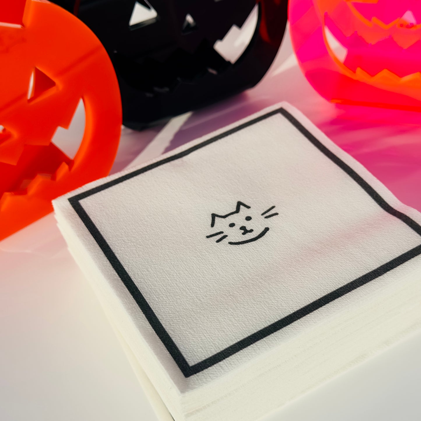 Halloween-themed paper napkins with a cat face design surrounded by colorful jack-o-lantern napkin holders on a table
