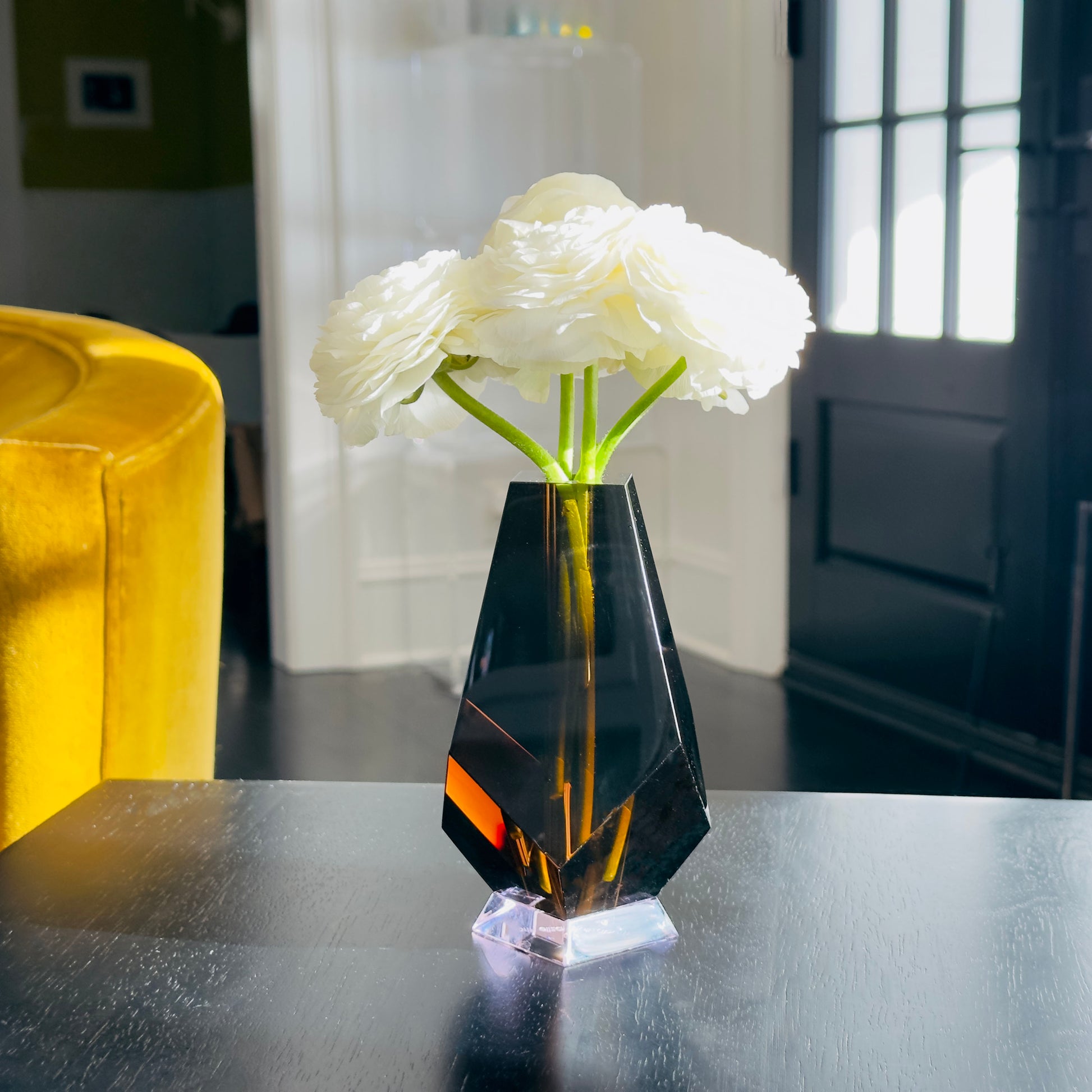 Black geometric vase with white flowers on a reflective surface