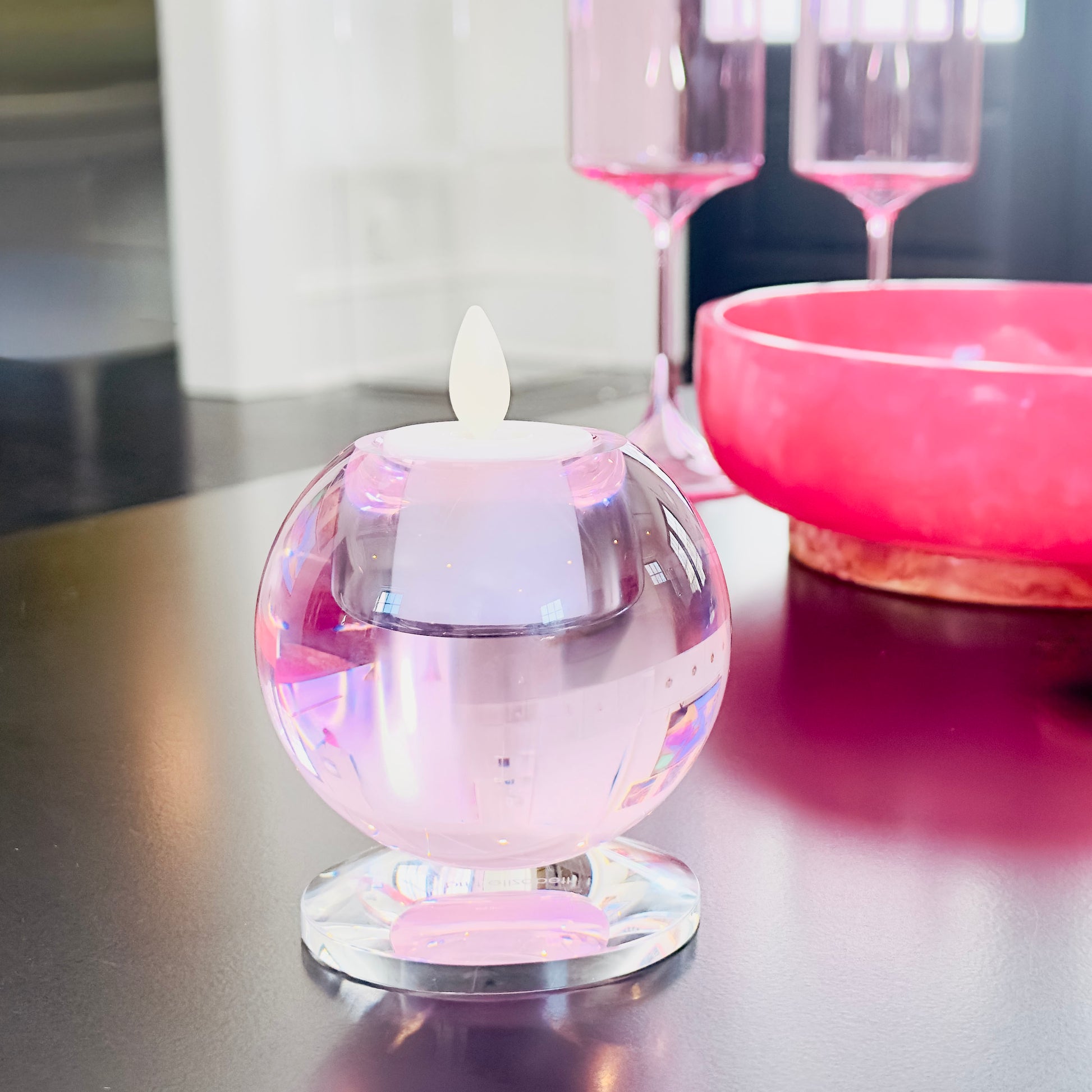 Small crystal candle holder with a white votive candle inside and sitting on a reflective table