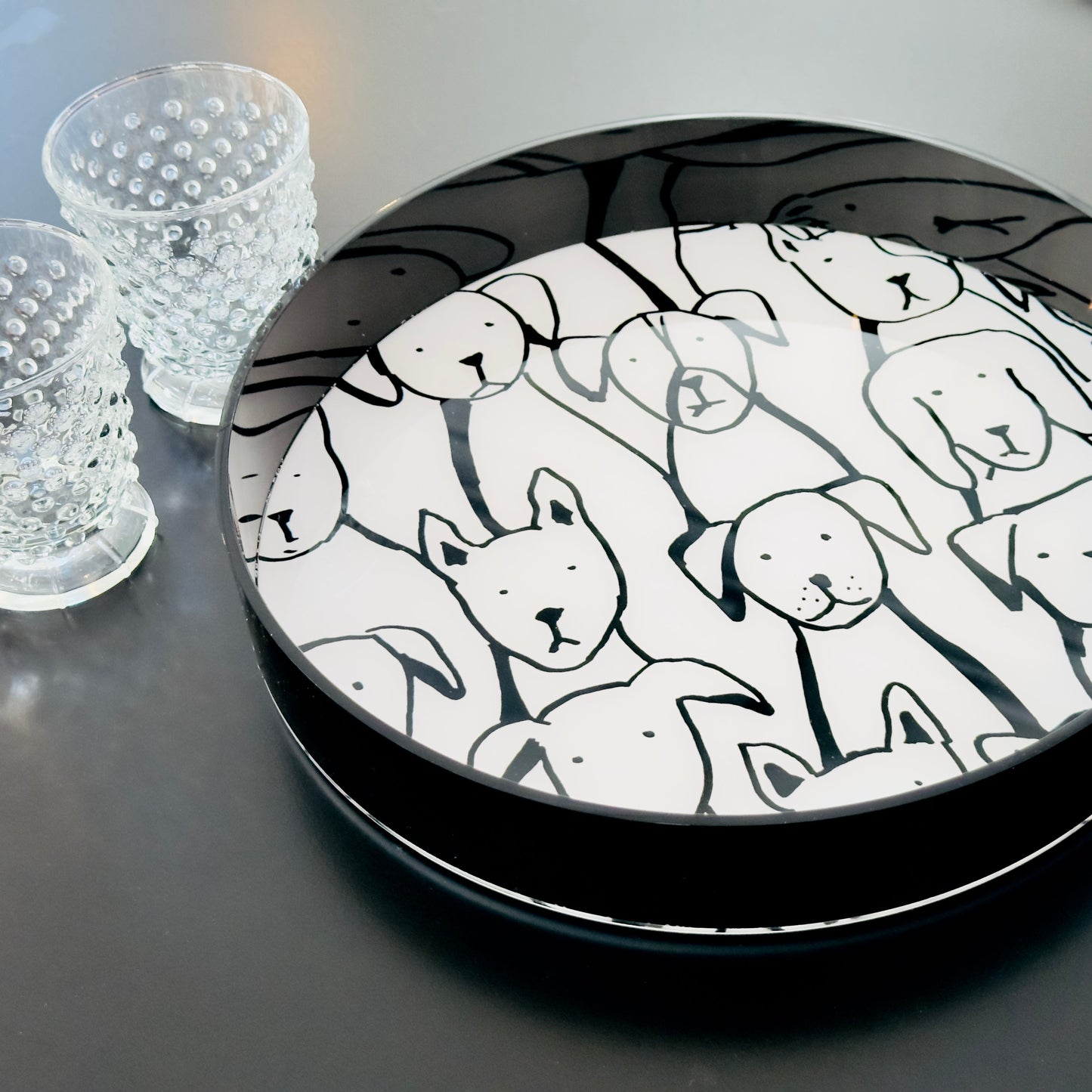 Round black tray with drawn dog faces pattern on a dark surface