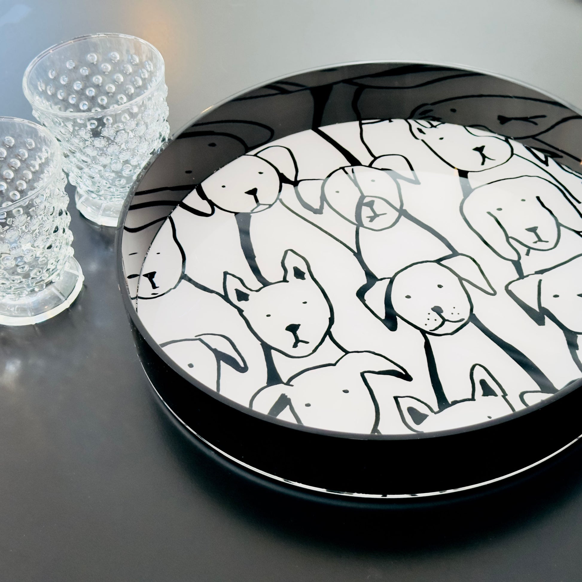 Round black tray with drawn dog faces pattern on a dark surface