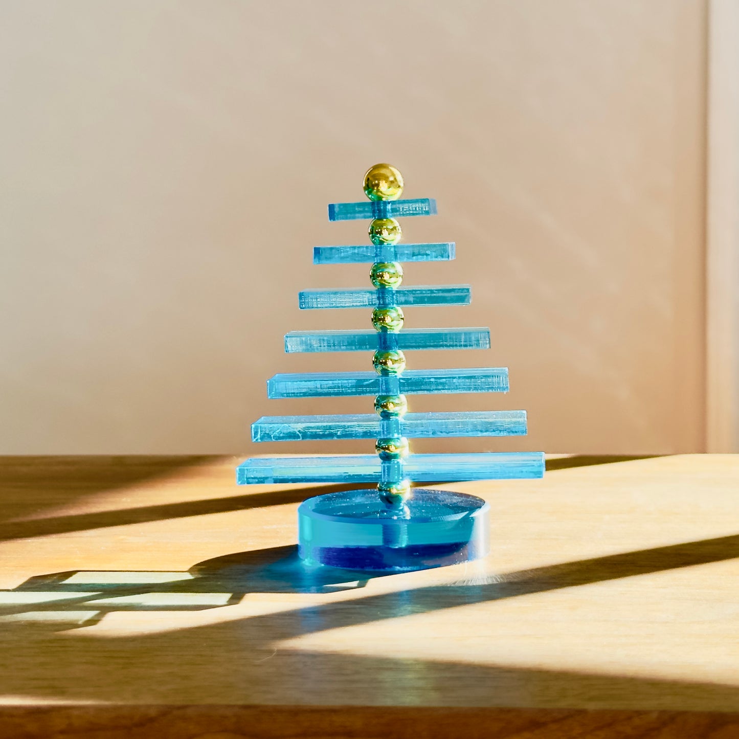 Blue acrylic Christmas tree with gold balls on a wooden surface