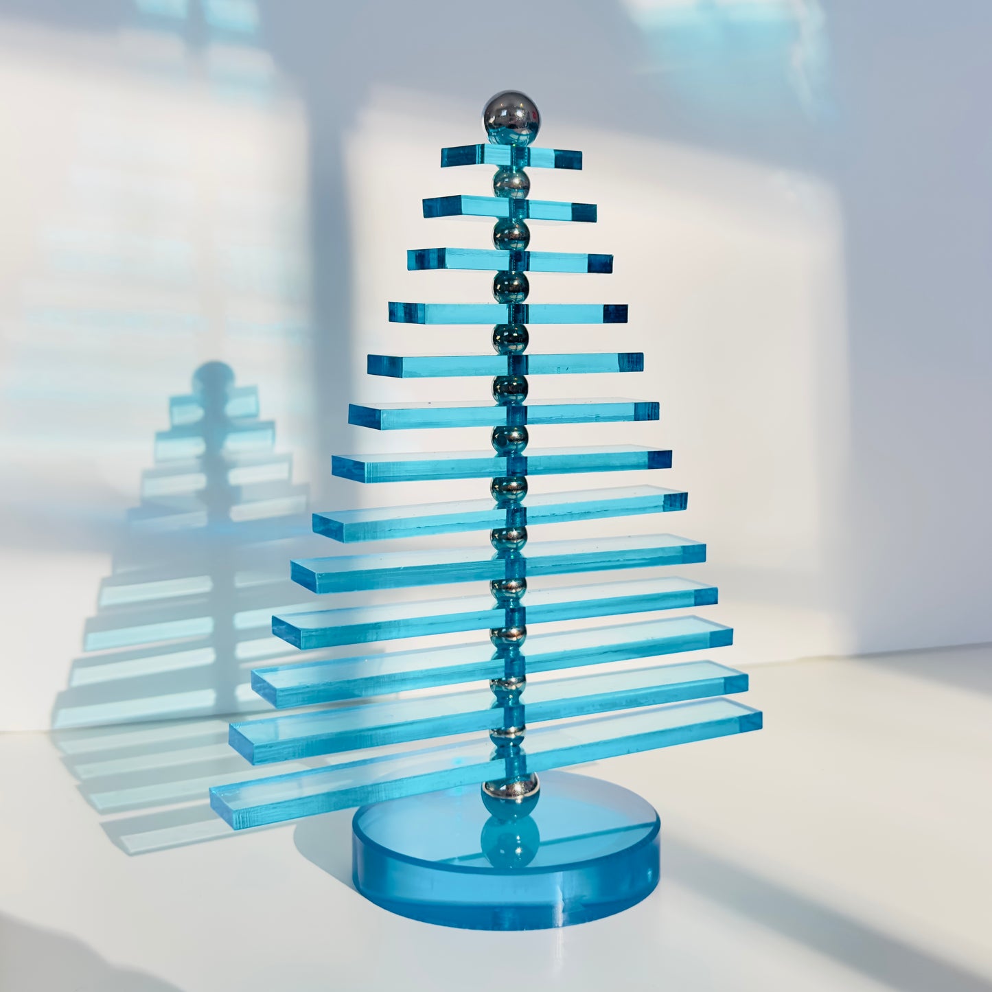 Blue acrylic sculpture with a reflective base on a white surface