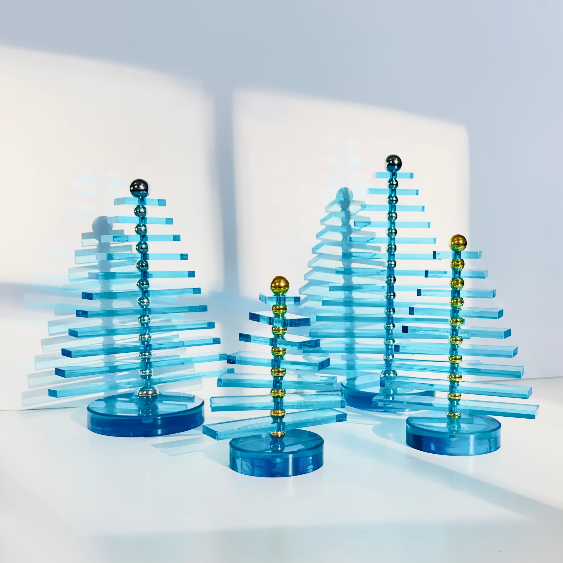 Set of four blue acrylic trees with gold and silver accents on a white background