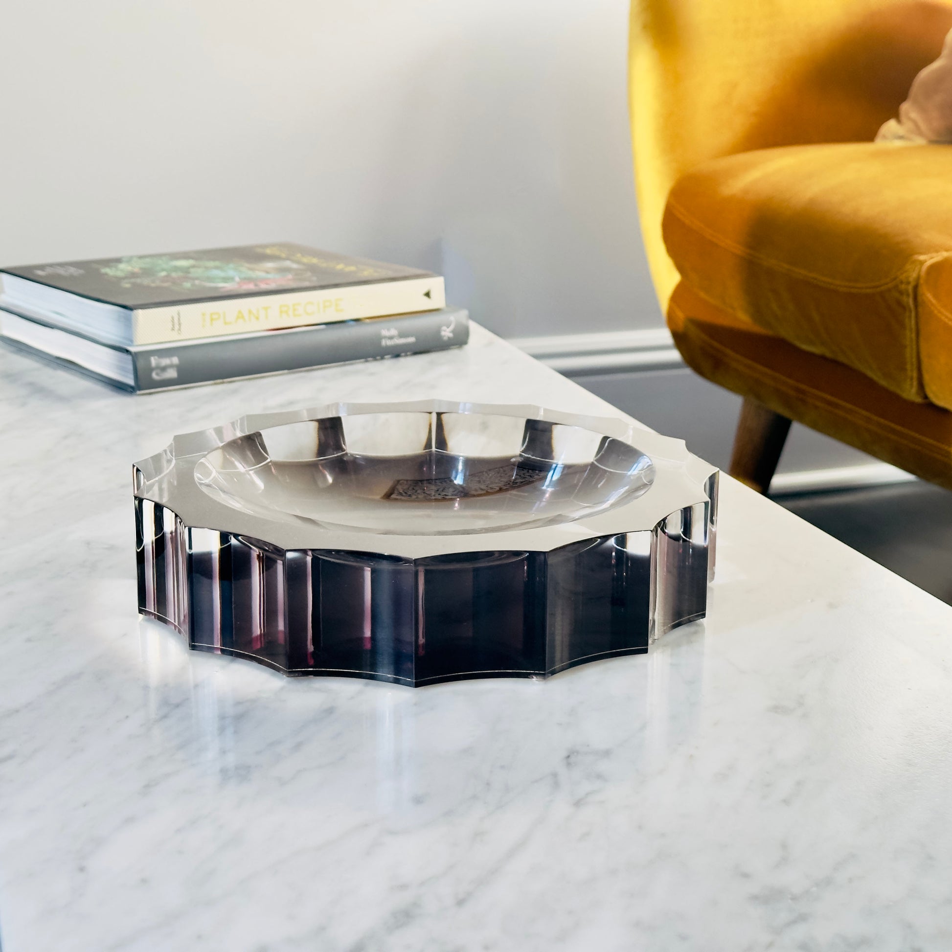 Decorative black bowl on a marble surface with books and a yellow chair in the background.