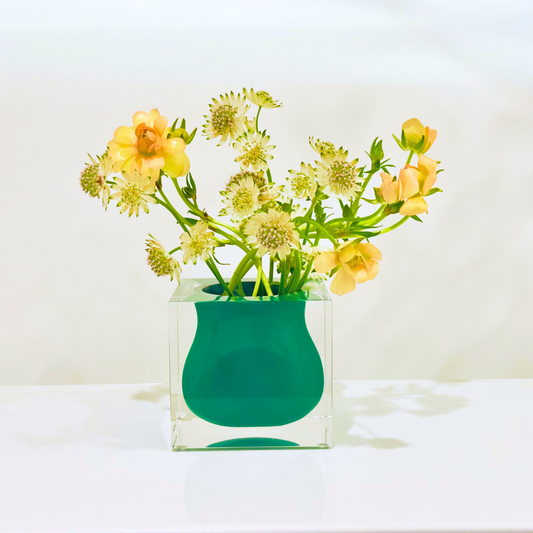Green vase with yellow flowers on a white surface