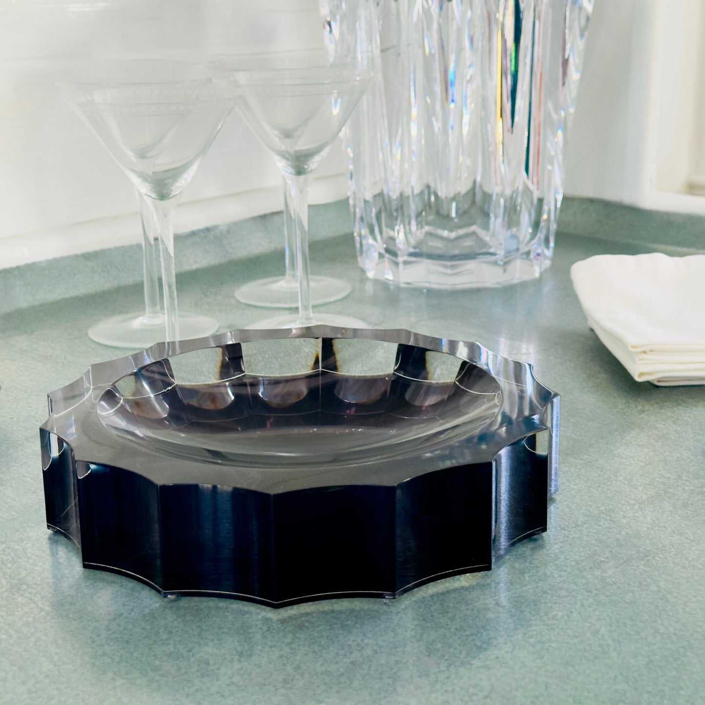 Decorative black and clear acrylic bowl  on a silver table with glasses in the background