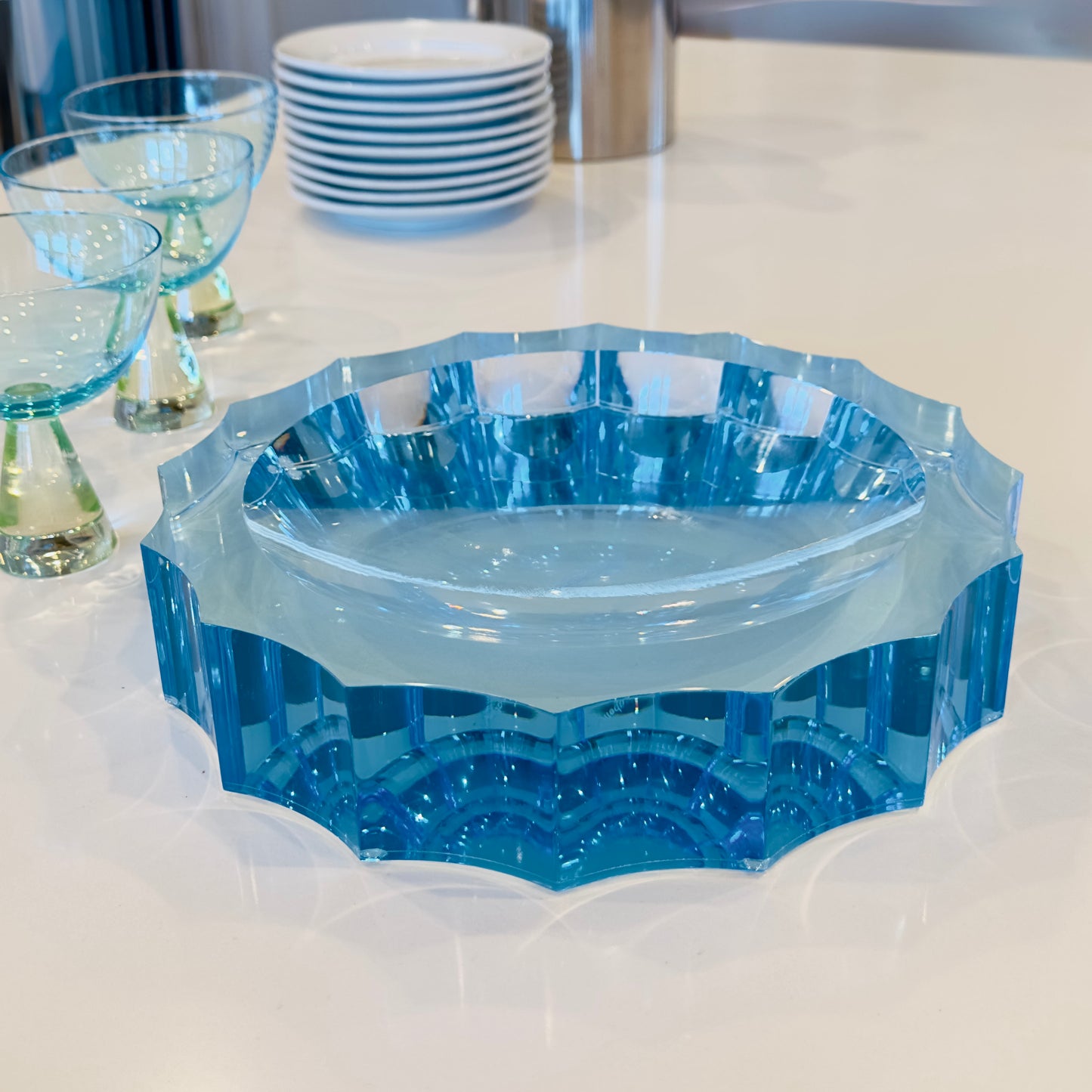 Blue acrylic bowl on a white surface with glasses and plates in the background