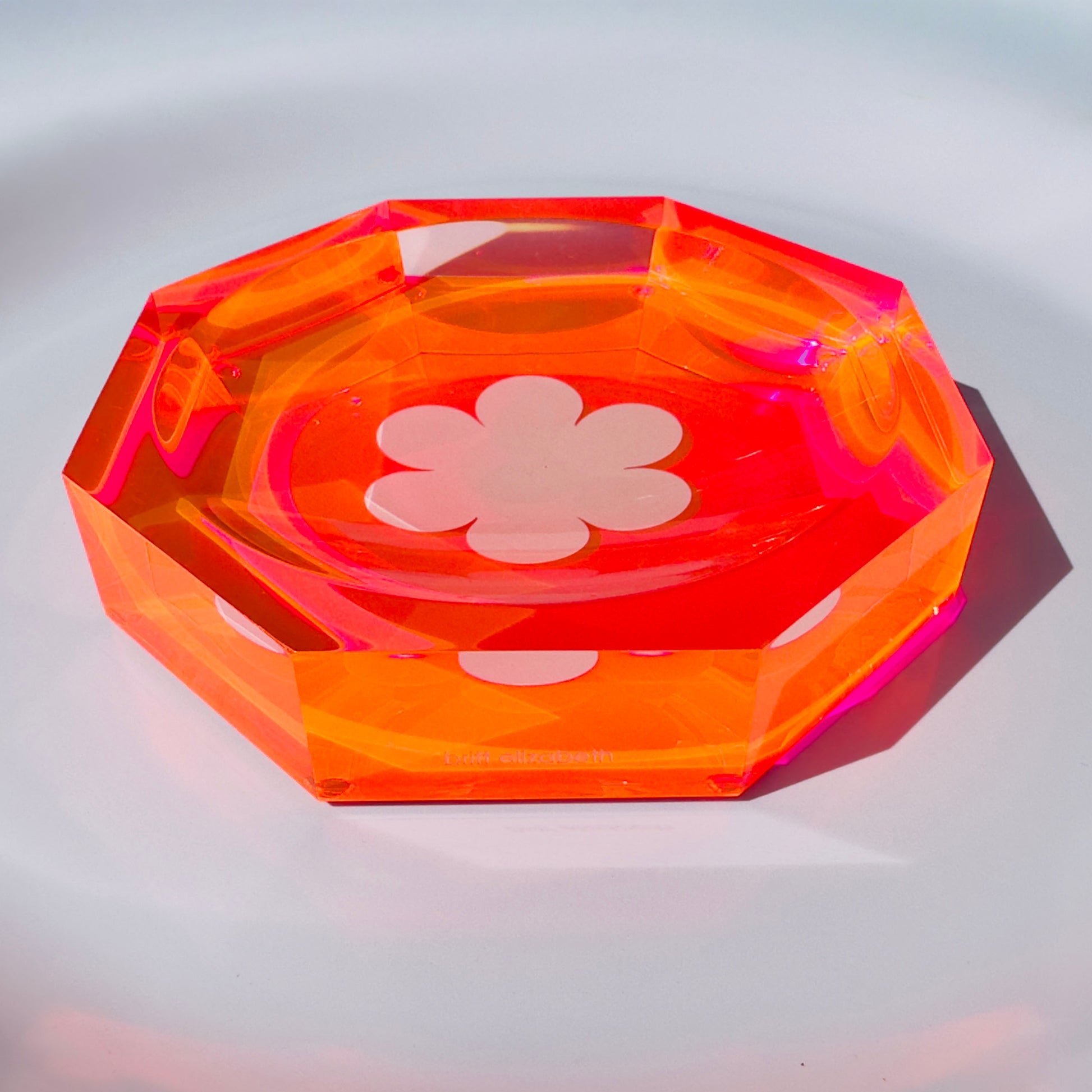 Octagonal transparent orange dish with a white flower design on a light gray background