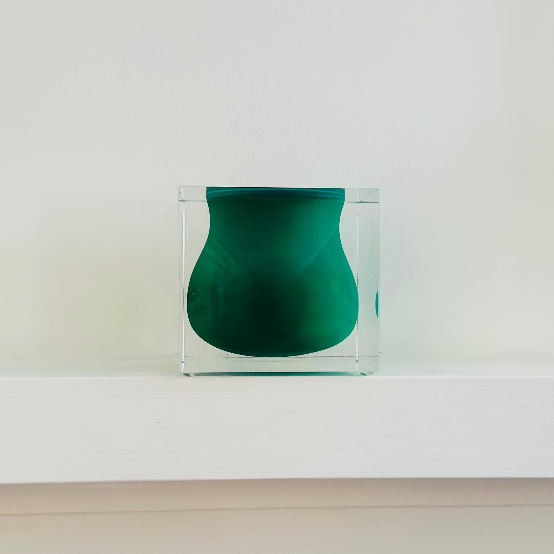 Green vase inside a clear glass box on a white surface with a light gray background